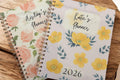 Two planners with floral designs on a wooden surface